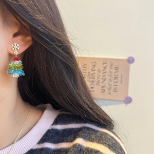 Close-up of handmade beaded Christmas tree earrings with colorful crystals and snowflake stud