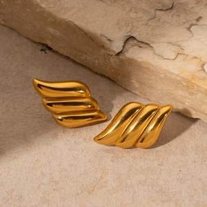 Macro shot of 18k gold plated wave design stainless steel stud earrings on beige stone