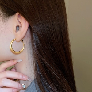 Close-up of gold plated round hoop earring with brushed metal texture on a female model