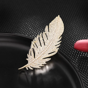 Elegant gold feather brooch with zircon stones on a reflective black display stand