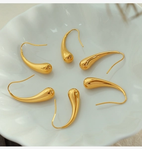 Six gold teardrop hook earrings arranged in a decorative white scalloped ceramic dish
