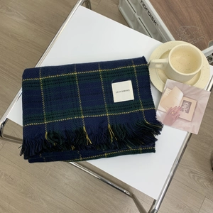 Folded blue and green plaid vintage scarf with fringe and label on a coffee table