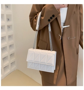 Close-up of white quilted chain bag with geometric embroidery on a brown suit model