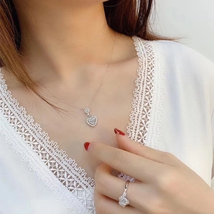 Detail view of heart-shaped silver jewelry set with zircon necklace and ring on model