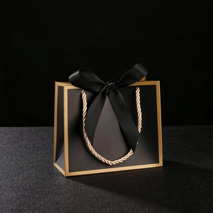 Detail of luxury black paper gift bag with gold trim and large decorative ribbon bow