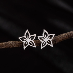 Détail de boucles d'oreilles fleurs ajourées en acier inoxydable sur fond de branche