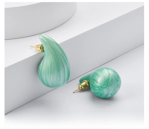 Close-up of mint green teardrop earrings with brushed marble texture on white background