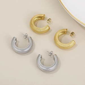 Detailed view of gold and silver C-shape earrings with a textured fish scale weave design