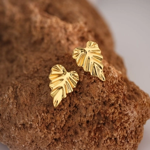 Macro shot of gold leaf stud earrings with detailed metallic veins on natural stone base