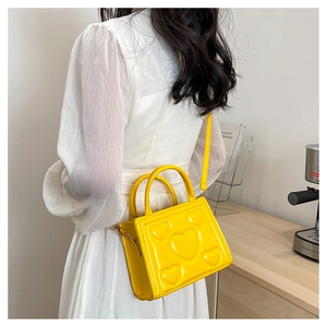 Détail du sac à bandoulière jaune brillant avec motif cœur sur une robe blanche