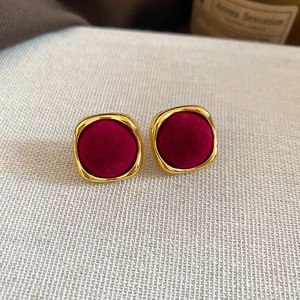 Detail of square gold earrings with deep red velvet inlay on beige fabric background