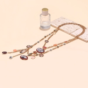 Close-up of layered gold necklace featuring enamel flower charms and elegant swan pendant