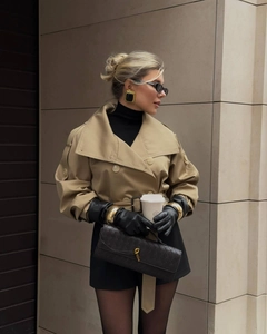 Détail du trench court kaki assorti de gants en cuir noir et d'une pochette tressée
