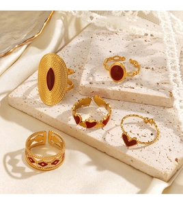 Close-up of gold minimalist rings with red heart patterns on a travertine surface