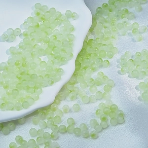 Detail of light green frosted glass beads for DIY jewelry making on white ceramic tray