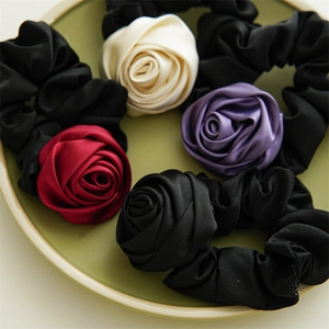Detail of satin rose scrunchies in black, white, purple and burgundy on a ceramic tray