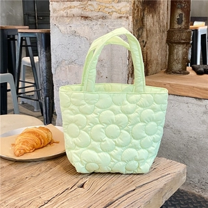 Detail of mint green quilted floral tote bag on a rustic wooden table with croissants