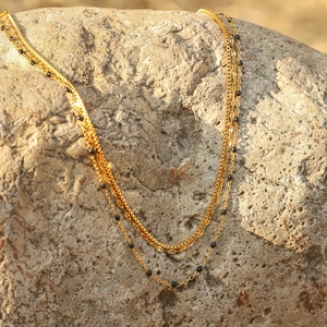 Three-layer gold stainless steel necklace with black beads on a natural stone background