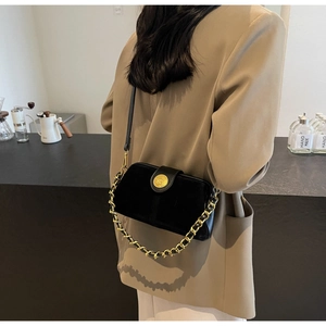 Close-up of black suede doctor bag with gold chain strap and circular embossed buckle