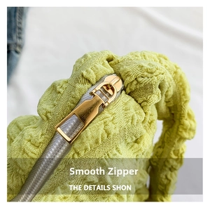 Close-up of golden metal zipper on light green popcorn texture ruched bag fabric