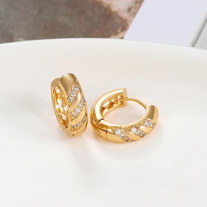 Detail of gold twisted hoop earrings with sparkling zircons on white ceramic tray
