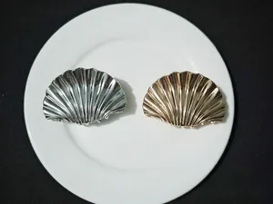 Top view of two shell-shaped metal hair claws in gold and silver finish on a plate