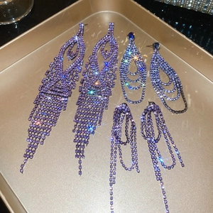 Detailed view of three pairs of purple rhinestone fringe earrings displayed in a metal tray