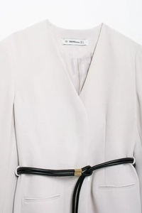 Detail view of V-neck blazer with thin black belt and golden buckle in off-white