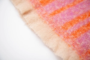 Close-up of soft plush scarf fabric featuring orange and pink stripes with fringed tassels