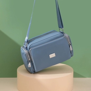 Bolso bandolera de nailon azul con correa ancha y múltiples bolsillos sobre un soporte
