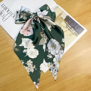 Detail of dark green satin bow hair clip with floral patterns on a wooden surface