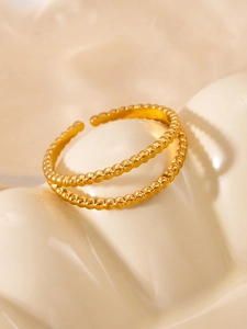 Detailed close-up of a double-layer golden beaded open ring on a textured ceramic surface
