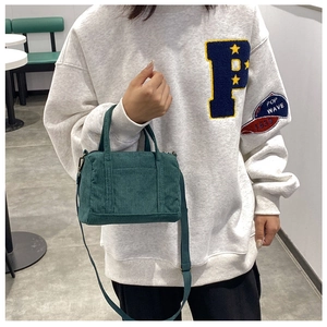 Green corduroy Boston bag shown as crossbody style in a cafe setting worn by a model