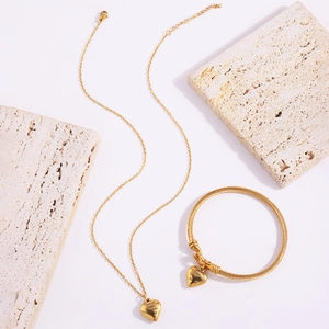 Detailed set of gold titanium necklace and heart engraved bracelet on stones
