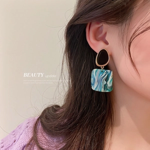 Detail of model wearing geometric earrings with blue marble resin and black oval studs