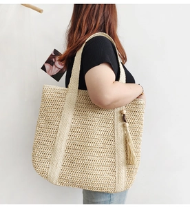 Detail of a beige woven straw tote bag with wood bead tassel hanging from the shoulder