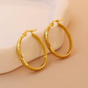 Detail of 18K gold plated hoop earrings with dragon scale texture on white ceramic