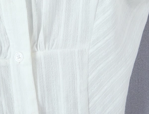 Macro detail of white textured jacquard fabric and a classic four-hole button on a polo shirt