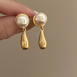 Close-up of elegant gold teardrop earrings featuring round white pearls and metallic pendants