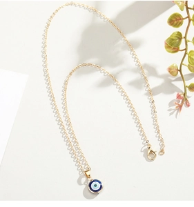 Close-up of golden Evil Eye pendant on a delicate chain with natural background elements