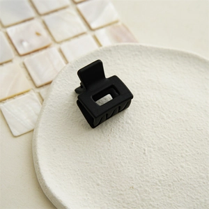 Close-up of a black matte square hair claw clip on a white textured ceramic plate