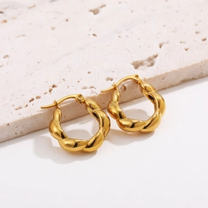 Macro view of gold twisted hoop earrings with irregular textured surface and glossy finish