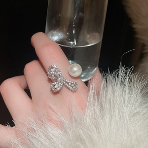 Close-up of a silver bow ring with white pearl and zircon crystals on a hand
