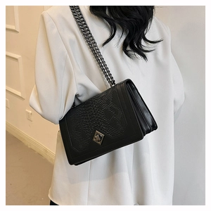 Detail of black crocodile texture bag with metal diamond lock and chain strap on model
