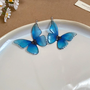 Detailed view of blue resin butterfly earrings with glitter wings on a white ceramic plate
