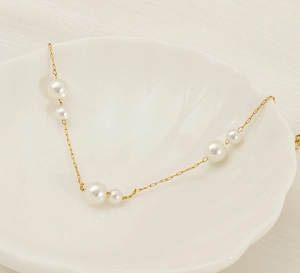 Detail of elegant gold pearl necklace displayed on a white shell-shaped ceramic plate