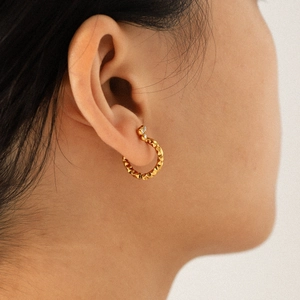 Hammered titanium steel gold hoop earrings with three zircon stones on a female model