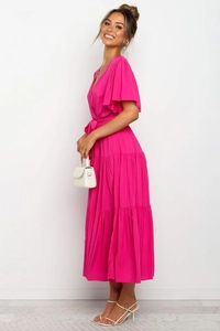 Detalle de vestido largo rosa fucsia con cuello en V, mangas con volantes y falda de capas