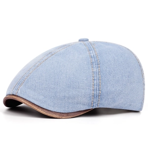 Detail of washed blue denim newsboy cap with brown leather brim stitching and visible seams