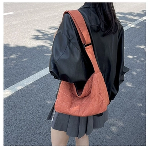Street style view of orange quilted dumpling bag with wide shoulder strap and large capacity